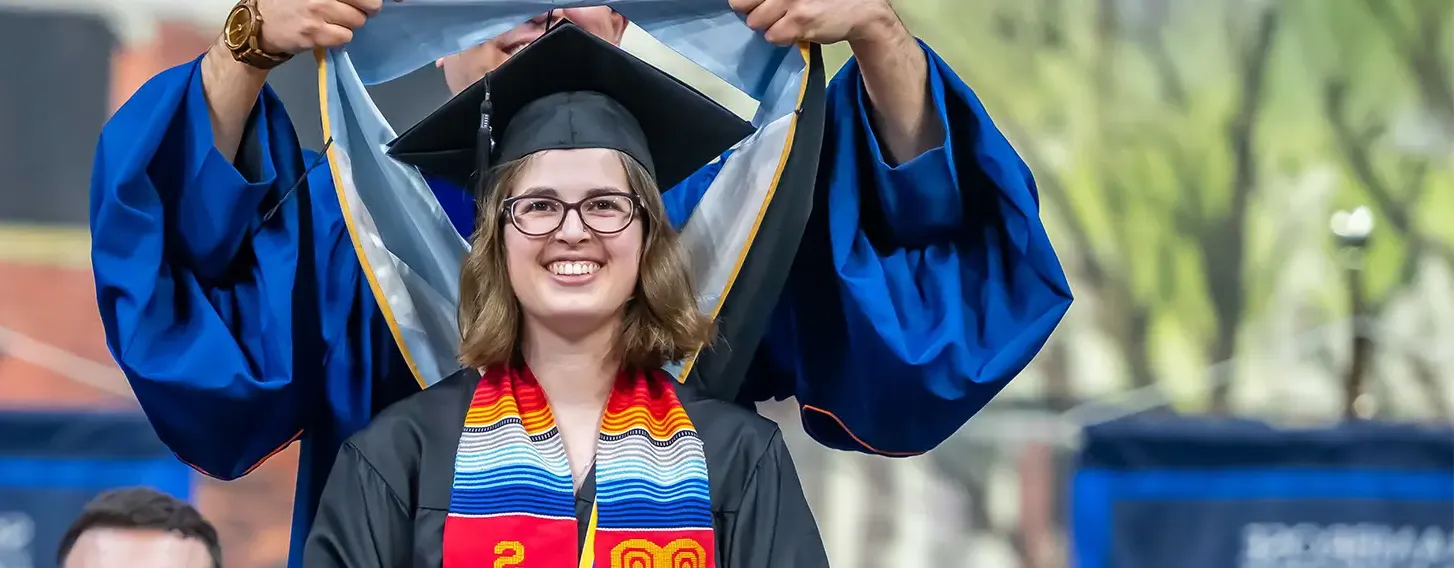 A smiling woman in a graduation cap and gown getting her masters hood.